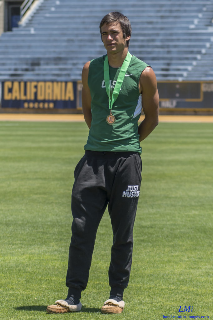 Athlete prepares for pole vault on a track with others watching.