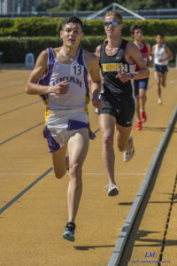 Two athletes sprinting on an indoor track during a race.