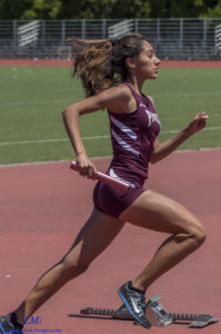 Female athlete sprinting on a track while holding a baton.