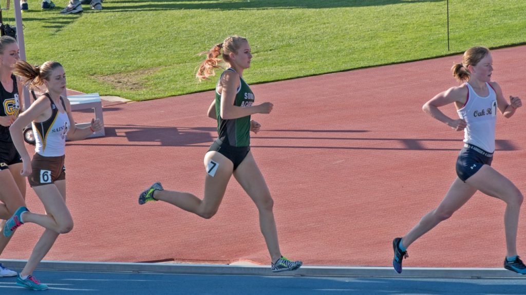 Athlete prepares for pole vault on a track with others watching.