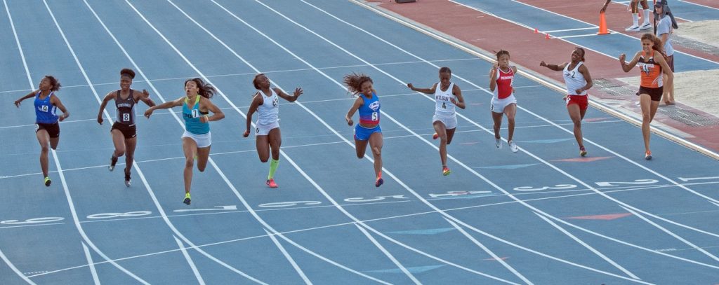 Athlete prepares for pole vault on a track with others watching.