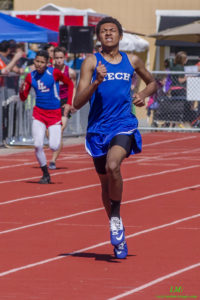 Athlete in blue sprinting ahead on a track during a race.
