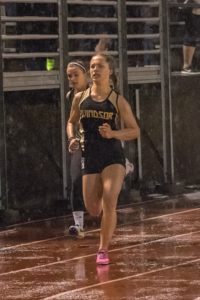 Athlete prepares for pole vault on a track with others watching.