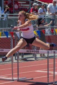 Athlete prepares for pole vault on a track with others watching.
