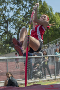 Athlete prepares for pole vault on a track with others watching.