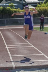 Athlete prepares for pole vault on a track with others watching.