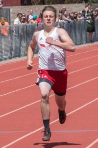 Young male athlete sprinting on an outdoor track in competition.