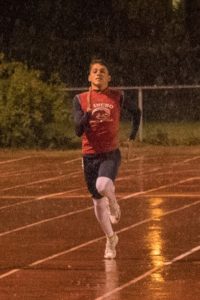 Athlete prepares for pole vault on a track with others watching.