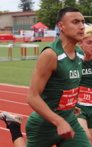Runners in green athletic uniforms competing on a track.