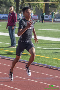 Athlete prepares for pole vault on a track with others watching.