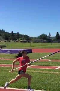 Young athlete in red shirt pole vaulting on a sunny day.