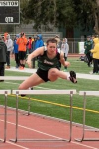 Athlete prepares for pole vault on a track with others watching.