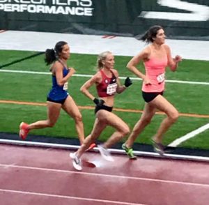 Athlete prepares for pole vault on a track with others watching.