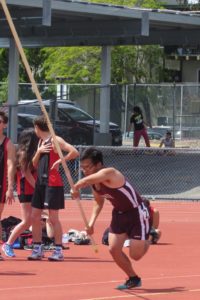 Athlete prepares for pole vault on a track with others watching.