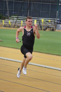 Athlete prepares for pole vault on a track with others watching.