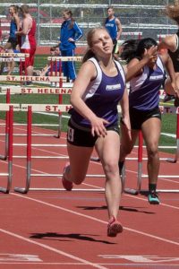 Two female athletes sprinting on a track during a hurdle race.