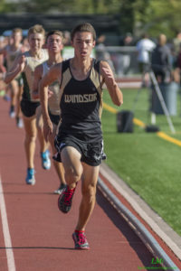 Athlete prepares for pole vault on a track with others watching.