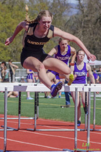 Athlete prepares for pole vault on a track with others watching.