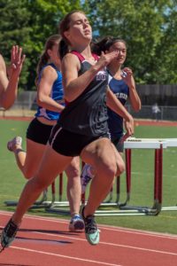 Athletes sprinting on a track during a hurdle race.