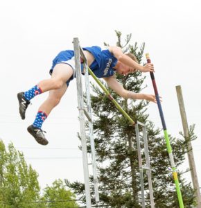 Athlete prepares for pole vault on a track with others watching.