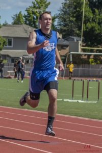 Athlete prepares for pole vault on a track with others watching.