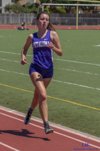 Athlete prepares for pole vault on a track with others watching.
