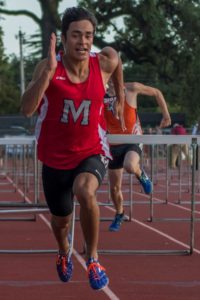 Athletes sprinting and jumping hurdles on a track during a race.