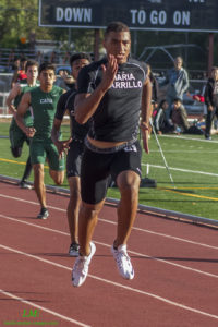 Athlete prepares for pole vault on a track with others watching.