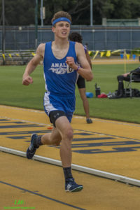 Athlete prepares for pole vault on a track with others watching.