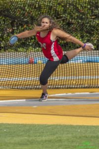 Athlete prepares for pole vault on a track with others watching.