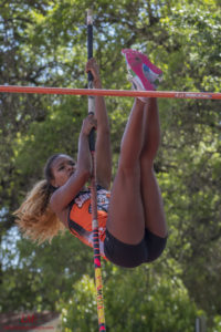 Female athlete pole vaulting outdoors, mid-jump.