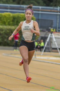 Athlete prepares for pole vault on a track with others watching.
