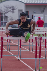 Athlete jumping over a hurdle during a race on a track.
