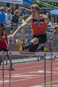 Athlete prepares for pole vault on a track with others watching.