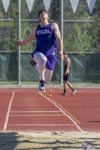 Athlete prepares for pole vault on a track with others watching.