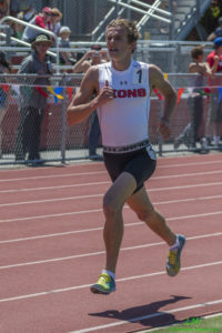 Athlete prepares for pole vault on a track with others watching.