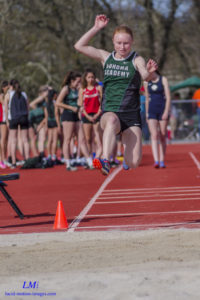 Athlete prepares for pole vault on a track with others watching.