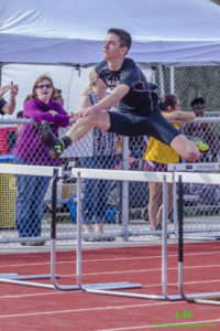 Athlete prepares for pole vault on a track with others watching.
