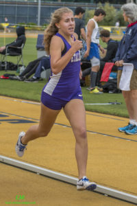 Athlete prepares for pole vault on a track with others watching.