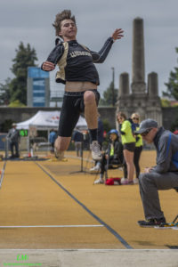 Athlete prepares for pole vault on a track with others watching.