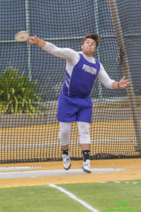 Athlete prepares for pole vault on a track with others watching.