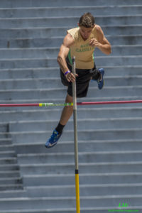 Athlete prepares for pole vault on a track with others watching.
