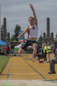 Athlete prepares for pole vault on a track with others watching.