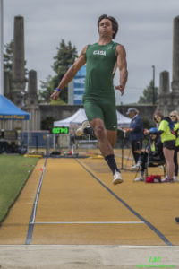 Athlete prepares for pole vault on a track with others watching.