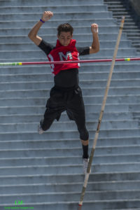 Athlete prepares for pole vault on a track with others watching.