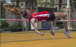 Athlete prepares for pole vault on a track with others watching.