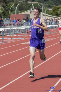 Athlete prepares for pole vault on a track with others watching.