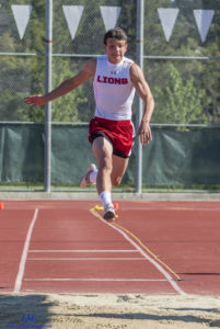 Athlete prepares for pole vault on a track with others watching.