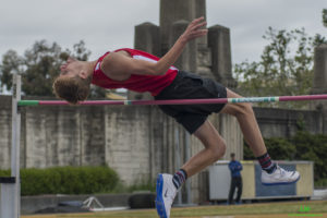 Athlete prepares for pole vault on a track with others watching.