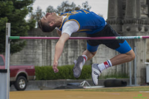 Athlete prepares for pole vault on a track with others watching.